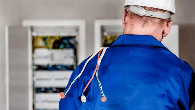 An electrician in a hard hat working at an electrical panel