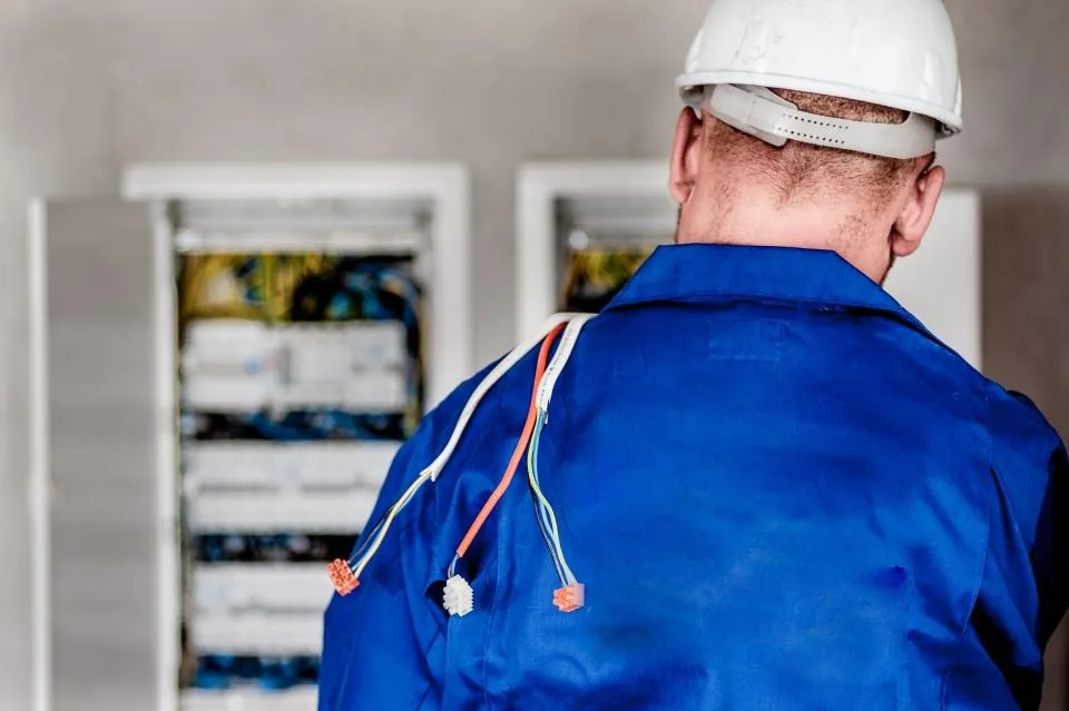 An electrician in a hard hat working at an electrical panel