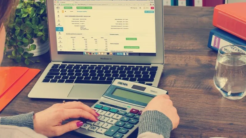 Hands using a calculator beside a laptop showing a spreadsheet