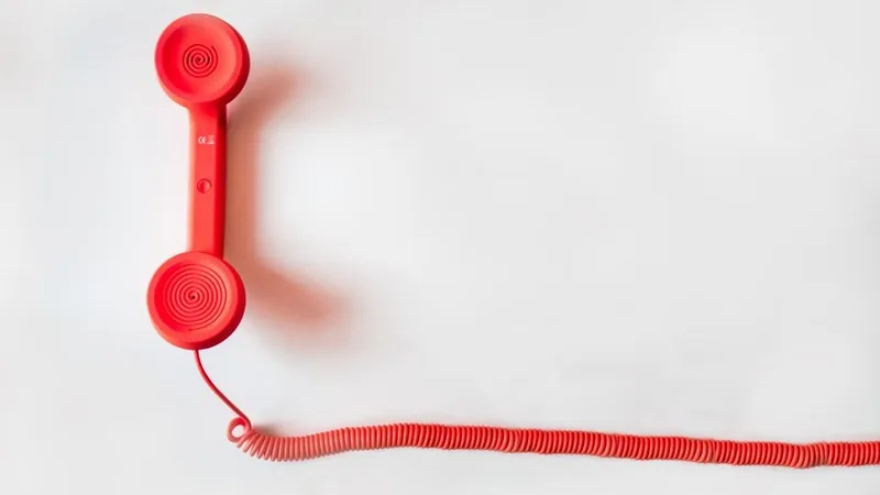 A red telephone handset with a coiled cord on a white background