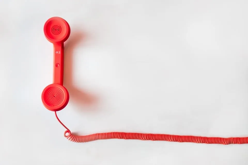 A red telephone handset with a coiled cord on a white background