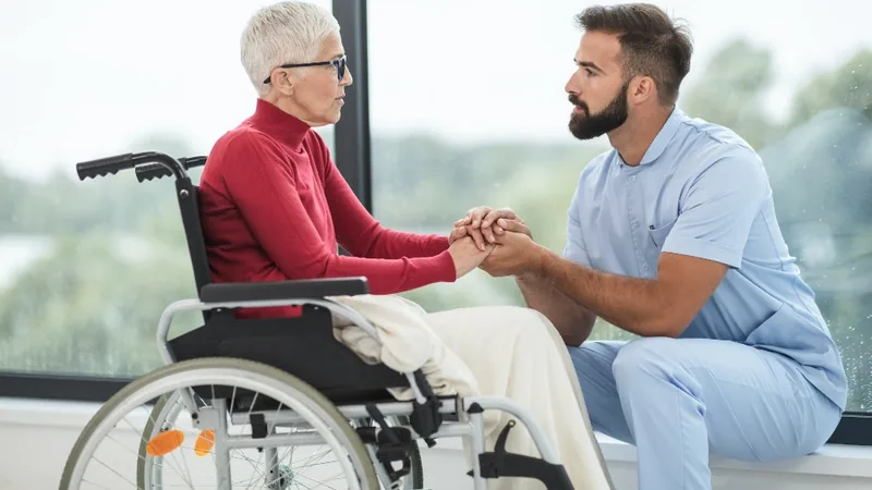 A carer holding hands with an older woman in a wheelchair