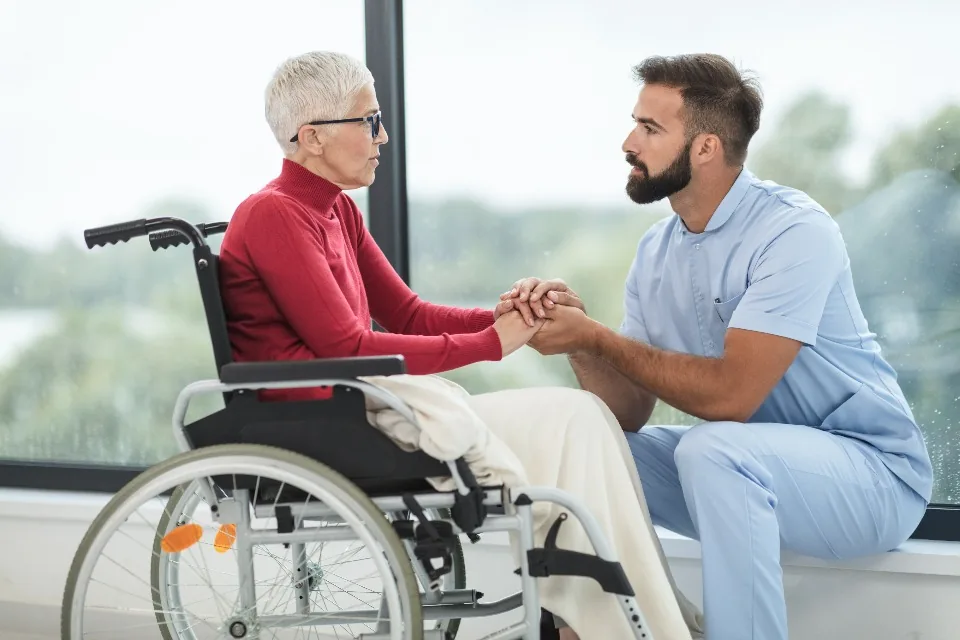 A carer holding hands with an older woman in a wheelchair